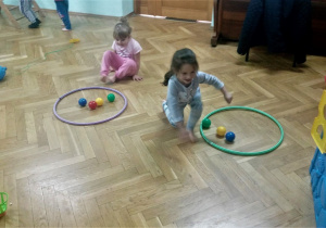 Dziewczynki z grupy "Żyrafki" wrzucają kolorowe piłeczki do koszyków.